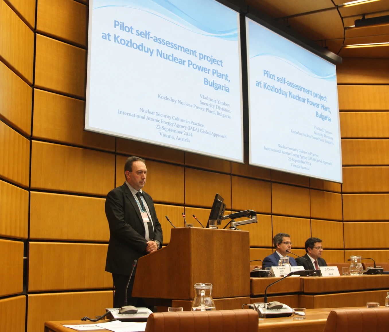 Vladimir Yankov speaking at an IAEA seminar in Vienna, with the presentation's title slide displayed on two screens